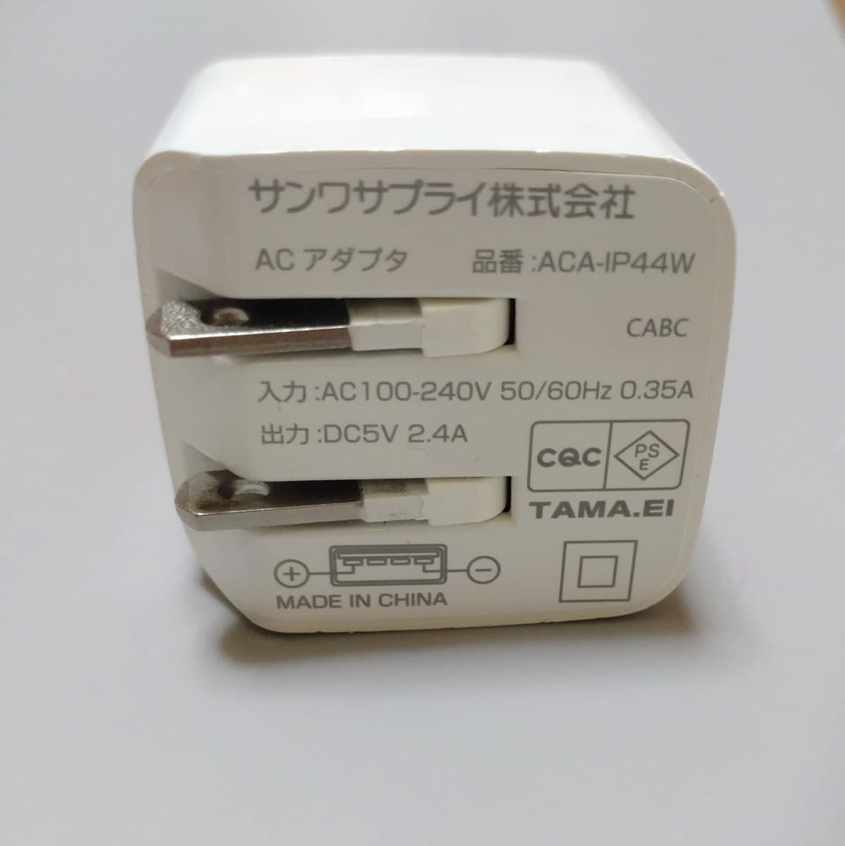 白い充電器の裏面。折りたたんだコンセントの端子が2本見え、サンワサプライ株式会社、ACアダプタ、品番ACA-IP44W、入力AC100-240V、出力DC5V2.4Aと印刷されている
