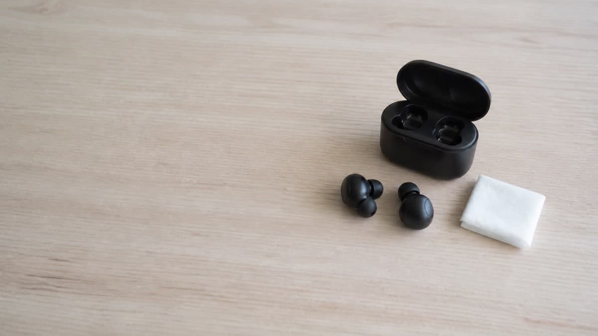 黒い充電ケースから取り出された左右独立型イヤホンと、拭くためのウェットティッシュ