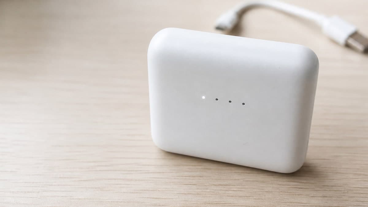 机の上に置かれた手のひらほどの白いモバイルバッテリー。側面に粒のような小さな丸いランプが4つ横に並び、そのうち1つだけがぼんやり灯っている。数字の表示はどこにも無い